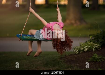 Young red headed girl hanging upside on a tree swing Stock Photo