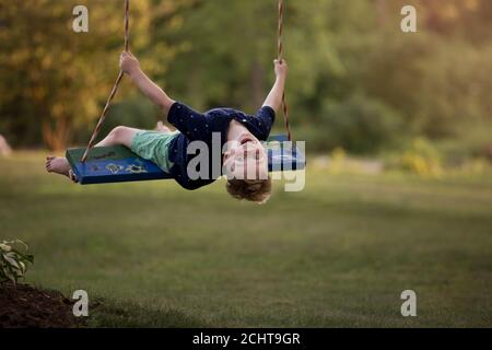 Young blond boy swinging on a wooden swing Stock Photo