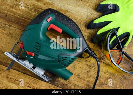 A jigsaw power tool, protective glasses, gloves and blades for electric jigsaw on old wooden background. Stock Photo