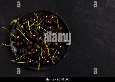 Fresh sour cherries in a black bowl on the dark background with copy space for text. Fresh ripe sour cherries. Top view. Stock Photo