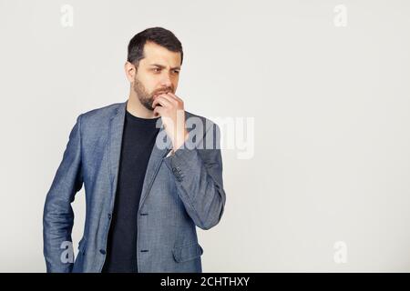 Male businessman with a beard, looks tense and nervous with his hands on his mouth biting his nails. Anxiety problem. Portrait of a man on a gray background. Stock Photo