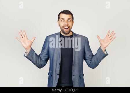 Young businessman man with a beard in a jacket, celebrating crazy and amazed with success with raised hands and open eyes, shouting excitedly. Winner concept. Portrait of a man on a gray background. Stock Photo