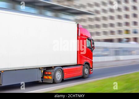 Red truck on blurry asphalt road over blue cloudy sky background Stock Photo