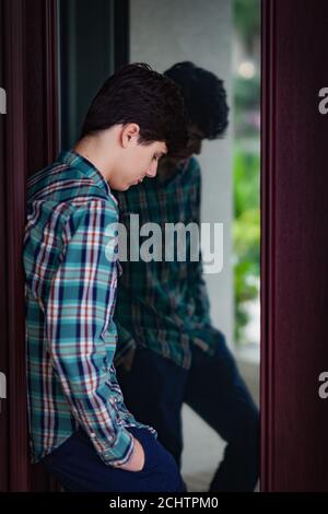 Teen boy leaning against door with reflection Stock Photo