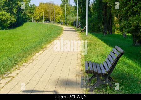 Picturesque green park with trees and grassy lawn with empty benches on the path Stock Photo