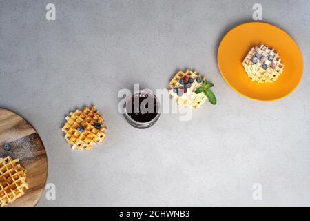 Round wooden chopping board with waffles filled with strawberry jam and blueberry with mint and blueberry on soft background Stock Photo