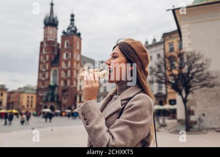 Woman eating bagel obwarzanek traditional polish cuisine snack on Market square in Krakow. Travel Europe in autumn Stock Photo
