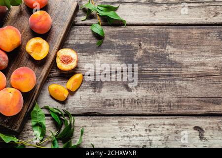 Peaches with leaves on dark wooden board with peach in halves. Composition with ripe juicy peaches Harvest for food. Fresh organic fruit Flat lay on Stock Photo