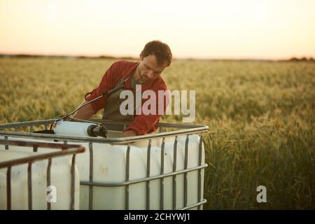 Portrait of male worker washing tools and equipment while standing by water tank in field at sunset, copy space Stock Photo