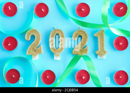 Xmas, winter, new year concept - Blue Christmas background with frame of little round red candles and gold numbers 2021 in center entwined with green Stock Photo