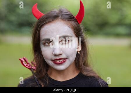 Close up portrait of smiling teenage girl wearing devil costume and face paint looking at camera outdoors Stock Photo