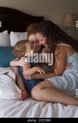 Mother and Young Children Cuddling and Playing Together on a Bed Stock Photo