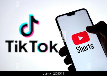 Youtube Shorts app logo seen on the silhouette of smartphone in a hand and TikTok logo on the blurred background. Real photo, not a montage. Stock Photo