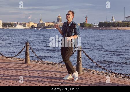 Man 20 years old is dancing on the waterfront of Neva river during trip in Saint-Petersburg. Young male is travelling over Russia. Stock Photo