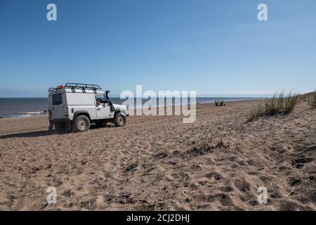 Grey beach patrol Land Rover 90 station wagen being driven along the sandy beach by Anderby, on the Linclonshire coast line, England. Stock Photo