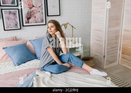 Young woman studying at home in the lounge sitting on the floor leaning against a sofa working with laptop and book Stock Photo