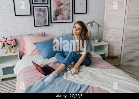 Young woman studying at home in the lounge sitting on the floor leaning against a sofa working with laptop and book Stock Photo