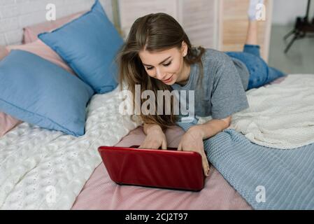 Young woman studying at home in the lounge sitting on the floor leaning against a sofa working with laptop and book Stock Photo