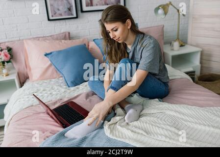 Young woman studying at home in the lounge sitting on the floor leaning against a sofa working with laptop and book Stock Photo