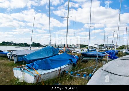 Small sailing or fishing boats on land with masts and covers on in Mudeford Quay, southern England, beautiful blue cloudy sky, many dingies stored on Stock Photo
