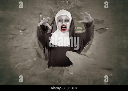 Scary devil nun coming out from a hole in the wall Stock Photo