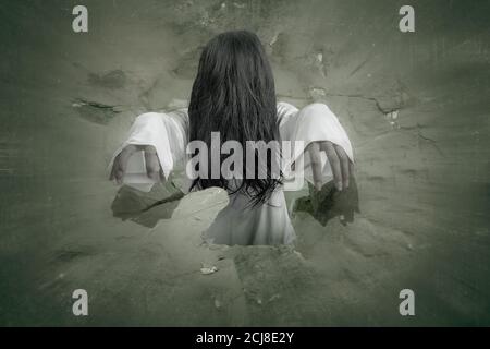 Scary ghost woman coming out from a hole in the wall. Halloween concept Stock Photo