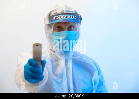 Man in a protective suit with an infrared thermometer gun in his hand Stock Photo