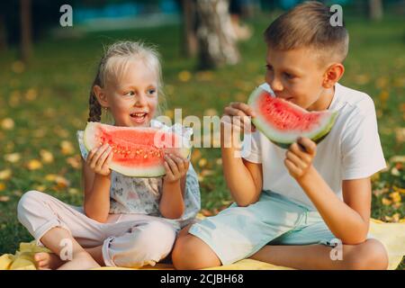 To cute kids lttle boy and girl eating juicy watermelon in the autumn park meadow Stock Photo