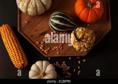 variety of pumpkins, squashes and gourds  as well as a dried a corn cob with kernels, randomly spread on a wooden plate black background. Ideal image Stock Photo