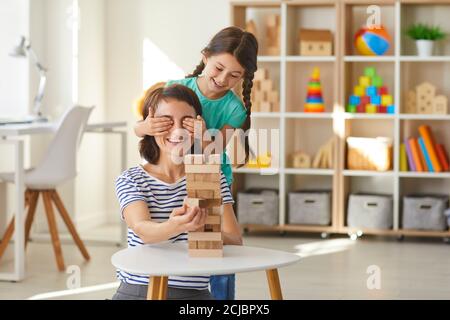 Little daughter putting hands over mommy's eyes while playing with wood blocks in modern nursery Stock Photo