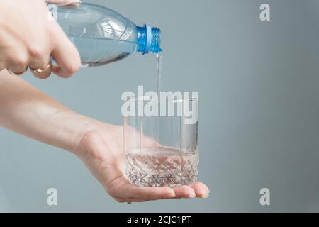 woman pouring water into a glass on gray background Stock Photo