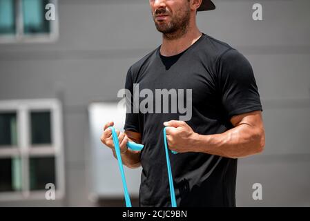 Fit muscular sports man doing bicep curl exercise with resistance band at home in the open air Stock Photo