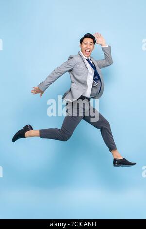 Full length fun portrait of happy energetic young Asian businessman jumping in mid-air isolated on studio blue background Stock Photo