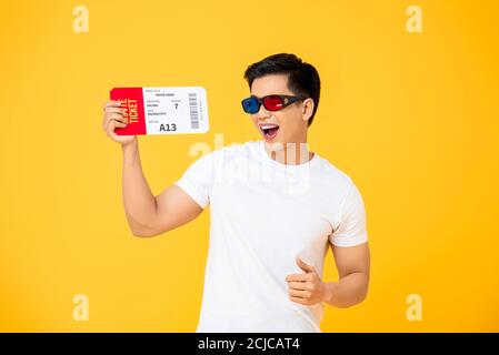 Waist up portrait of joyful young Asian man wearing 3D glasses holding movie ticket in isolated studio yellow background Stock Photo