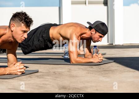 Group of athletic men doing plank morning workout exercise outdoors on rooftop floor Stock Photo