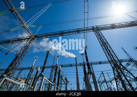 Power generating plant. Transformer substation with electric grids and electric High-voltage equipment on blue sky background. White smoke of factory Stock Photo