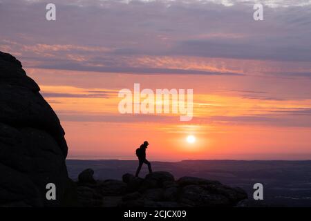 Man standing on Haytor rocks at sunrise silhoutted against a bright orange sky Stock Photo