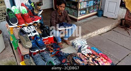 DISTRICT KATNI, INDIA - SEPTEMBER 22, 2019: An asian sales poor man showing footwear stuff into fashion outlet at local city street market place. Stock Photo