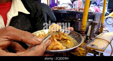 DISTRICT KATNI, INDIA - SEPTEMBER 24, 2019: an indian man having samosa on plate with spoon at street food carriage shop in market street. Stock Photo