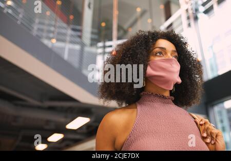 Young Mixed Race Businesswoman Wearing Face Mask In Modern Office Foyer During Covid-19 Pandemic Stock Photo