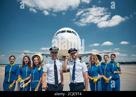 Cheerful airline workers standing in airfield under blue sky Stock Photo