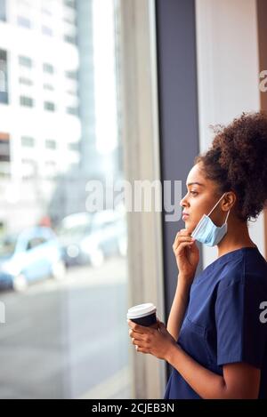 Overworked Nurse In Scrubs With Face Mask Takes Coffee Break In Busy Hospital During Health Pandemic Stock Photo
