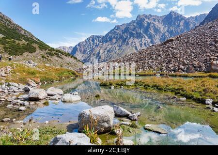 Idyllic summer landscape with hiking trail in the mountains with beautiful fresh green mountain pastures, river with reflection and clouds. Stock Photo