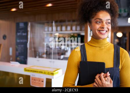 Portrait Of Female Business Owner Of Coffee Shop In Mask Using Digital Tablet During Health Pandemic Stock Photo