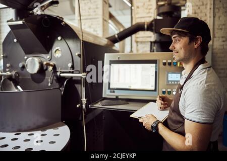 Handsome male worker using coffee roasting machine and taking notes Stock Photo