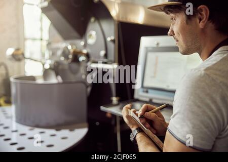 Male worker taking notes while using coffee roasting machine Stock Photo
