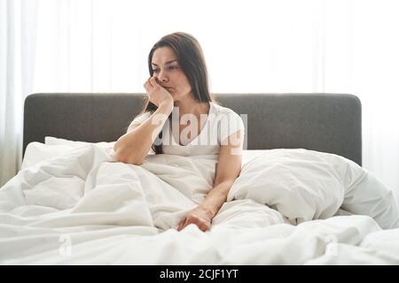 Sad thoughtful female sitting in a bedroom Stock Photo