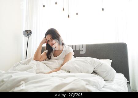 Upset young long-haired woman sitting in bed Stock Photo
