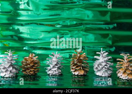 Metallic silver and gold pine cones at shiny green background. Copy space Stock Photo