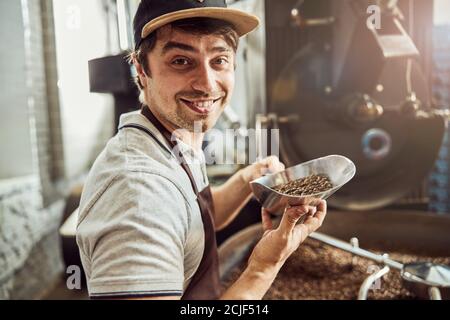 Joyful male worker holding scoop with coffee beans Stock Photo